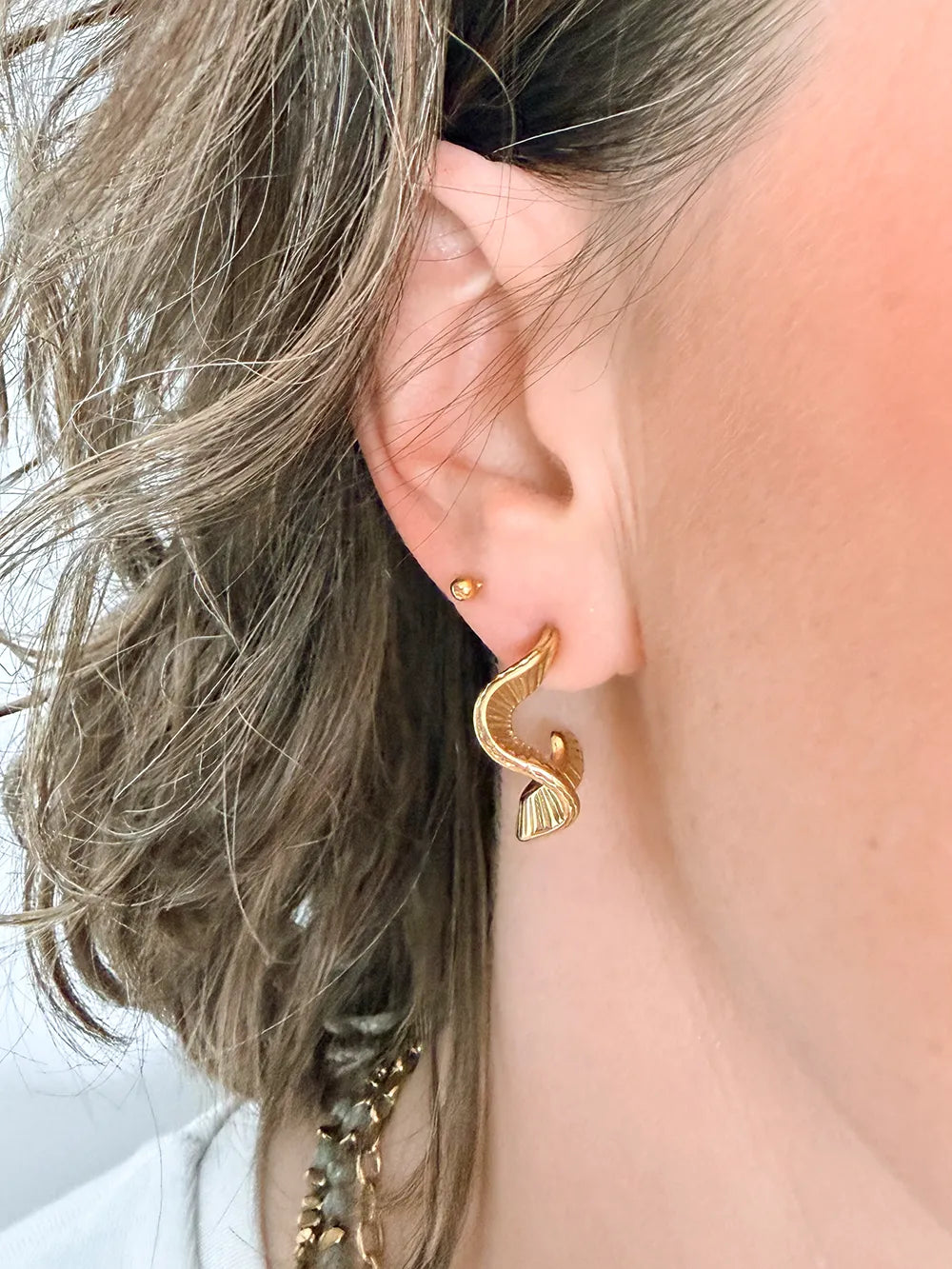 créoles petit formats de forme ondulé et striée de couleur doré porté par une femme