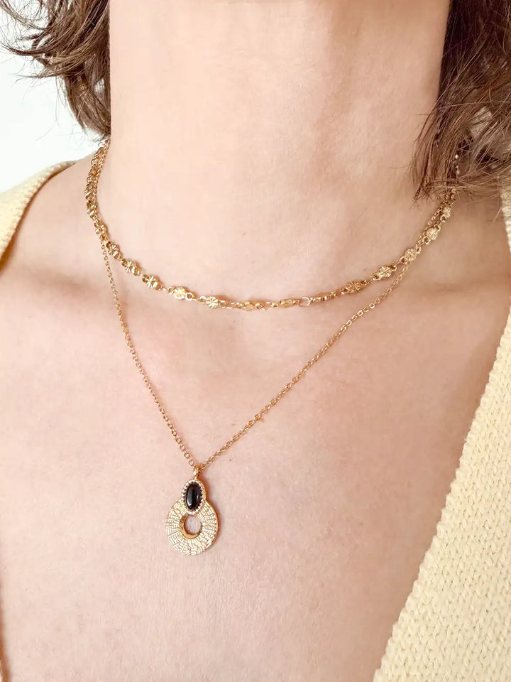 accumulation de colliers dorés sur femme avec un chaine étoilé et un pendentif cercle strié et pierre noire ovale