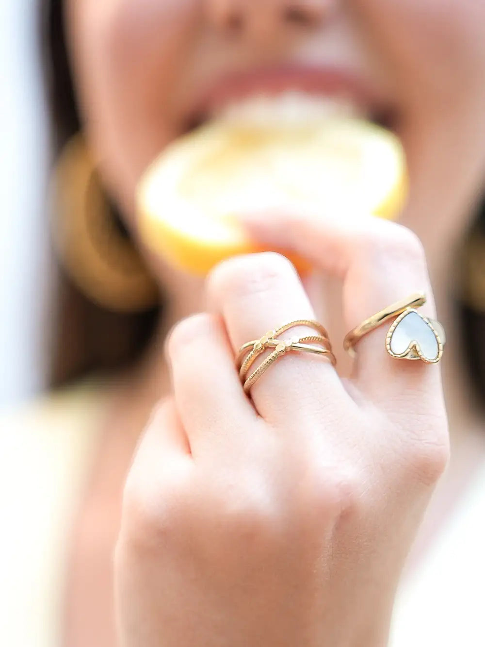 femme portant 2 bagues dorées en acier inoxydable avec une bague avec un coeur en nacre blanche.
