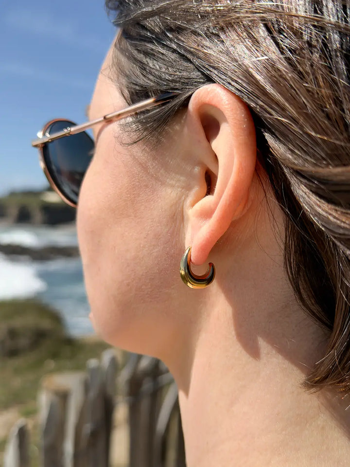 Boucles d’oreilles dorées en forme de goutte portées à l’oreille