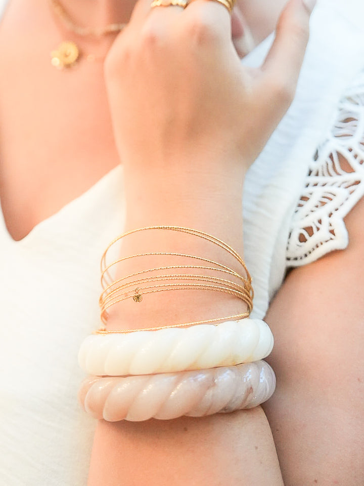 Femme portant des bracelets joncs large en résine rose poudré et blanc marbré ainsi que des joncs fin avec pampilles dorées.