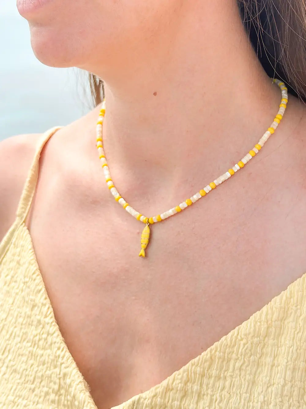 femme portant un collier perles jaunes et nacrées avec pendentif poisson doré